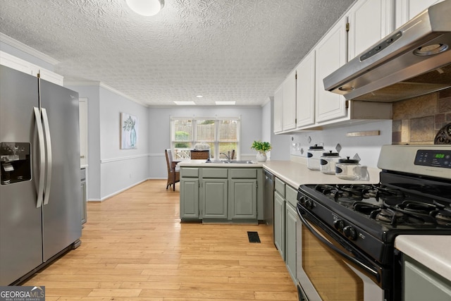 kitchen with a sink, ornamental molding, appliances with stainless steel finishes, light countertops, and under cabinet range hood
