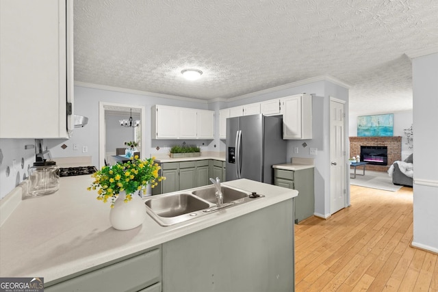 kitchen featuring a fireplace, stainless steel fridge, light countertops, and a sink