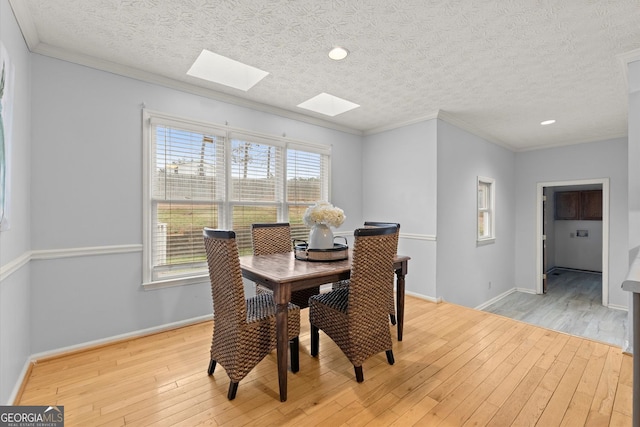 dining room featuring a skylight, baseboards, and light wood-type flooring
