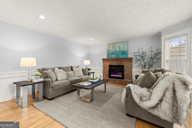 living room featuring wainscoting, ornamental molding, a textured ceiling, and light wood-style flooring