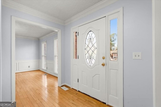 entryway with wainscoting, light wood finished floors, a textured ceiling, and ornamental molding