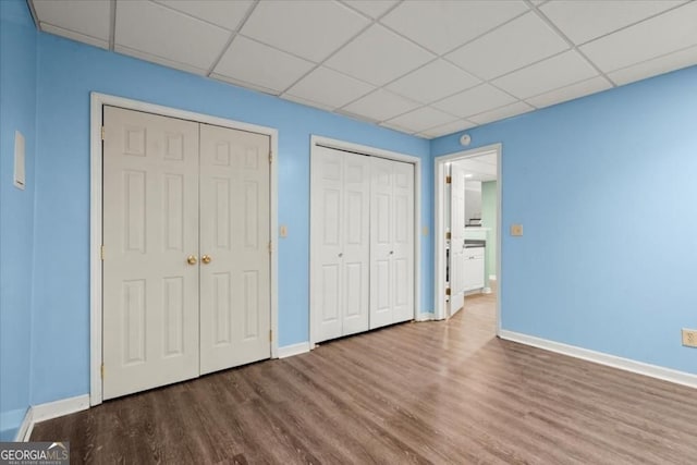 unfurnished bedroom with wood finished floors, a drop ceiling, and baseboards