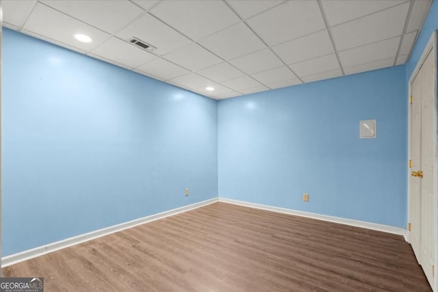 empty room featuring wood finished floors, visible vents, a drop ceiling, and baseboards