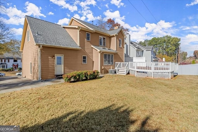 rear view of property with a lawn, central air condition unit, a deck, fence, and roof with shingles