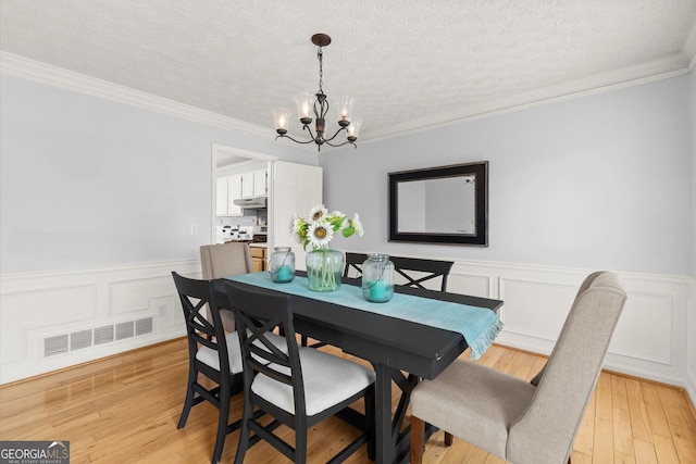 dining area with a notable chandelier, wainscoting, light wood-style floors, ornamental molding, and visible vents