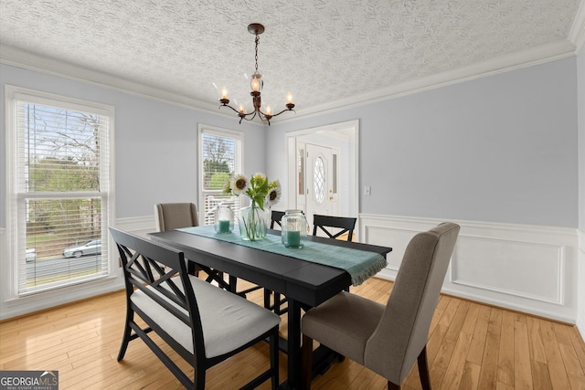 dining area featuring light wood finished floors, a wainscoted wall, an inviting chandelier, and crown molding