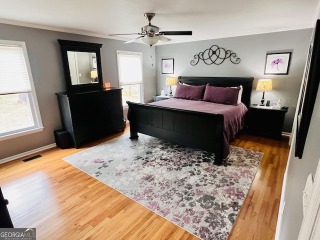 bedroom featuring a ceiling fan, baseboards, visible vents, crown molding, and wood finished floors