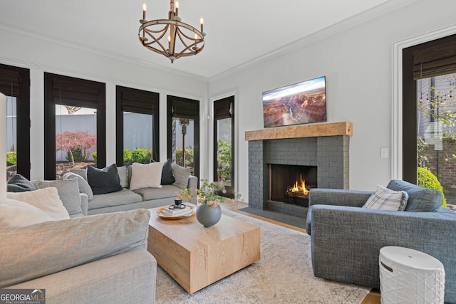 living room featuring a brick fireplace, a chandelier, crown molding, and wood finished floors
