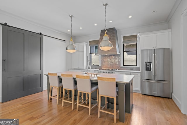 kitchen with high end refrigerator, a barn door, light countertops, decorative backsplash, and a center island with sink