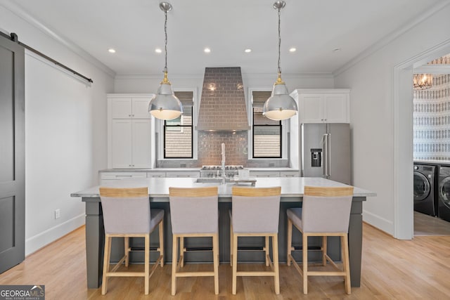kitchen featuring washer and clothes dryer, high quality fridge, a center island with sink, light countertops, and ornamental molding