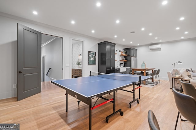 game room with a wall mounted air conditioner, light wood-style floors, baseboards, recessed lighting, and crown molding