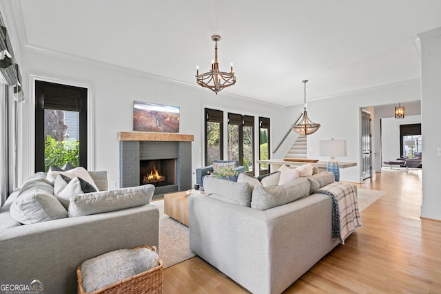 living room featuring stairs, light wood-style flooring, a fireplace, and a chandelier