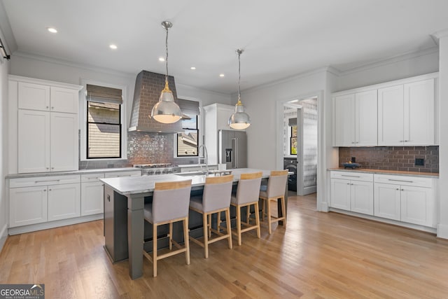 kitchen featuring high quality fridge, wall chimney exhaust hood, decorative backsplash, a sink, and crown molding