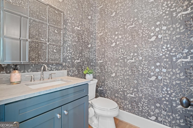 bathroom with wallpapered walls, toilet, wood finished floors, vanity, and baseboards