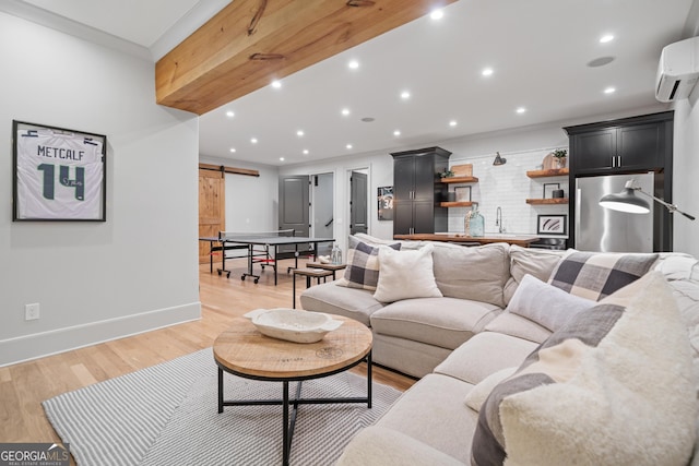living room featuring a barn door, a wall mounted air conditioner, baseboards, light wood-style flooring, and bar