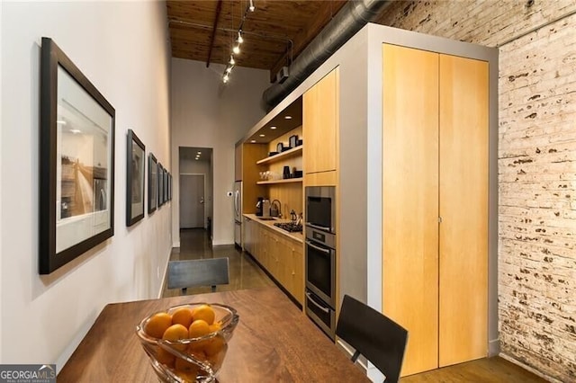 hall featuring a sink, a towering ceiling, brick wall, and dark wood-style floors