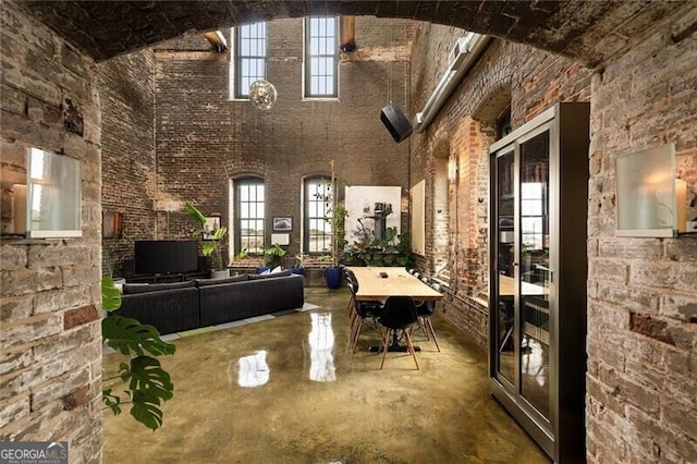 unfurnished living room with concrete floors, a high ceiling, and brick wall