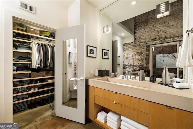 bathroom with brick wall, vanity, a spacious closet, and visible vents