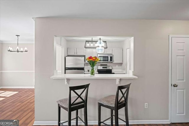 303 Mill Pond Ct SE, Smyrna, GA 30082 - kitchen featuring a kitchen breakfast bar, a peninsula, an inviting chandelier, stainless steel appliances, and dark wood-style flooring