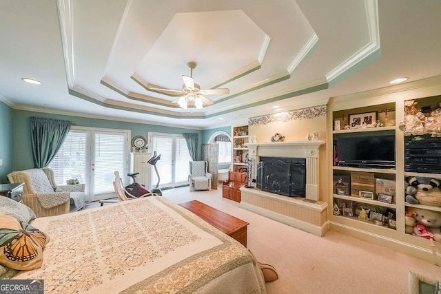 bedroom with carpet flooring, a fireplace with raised hearth, a raised ceiling, crown molding, and a ceiling fan