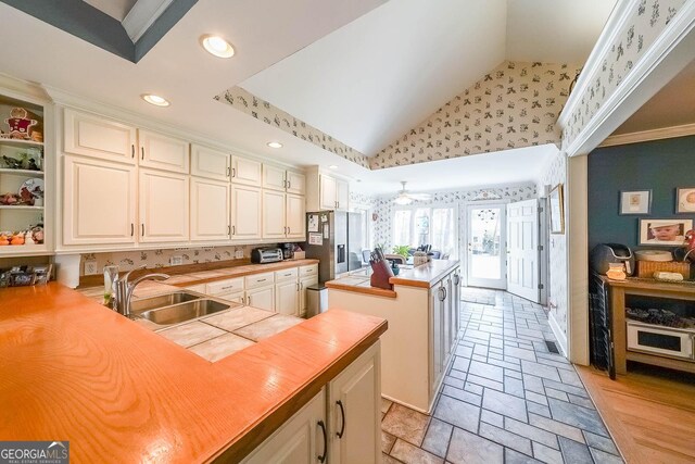 kitchen with a sink, stone tile flooring, a center island, vaulted ceiling, and stainless steel fridge