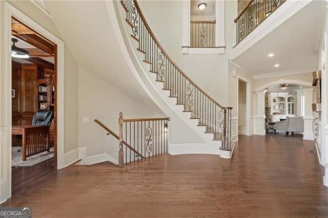 foyer entrance featuring crown molding, arched walkways, baseboards, wood finished floors, and ornate columns