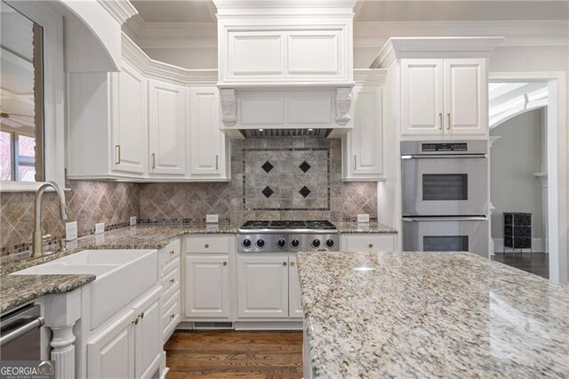 kitchen featuring appliances with stainless steel finishes, a sink, dark wood finished floors, white cabinetry, and ornamental molding