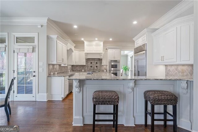 kitchen featuring backsplash, a kitchen bar, appliances with stainless steel finishes, a peninsula, and white cabinetry