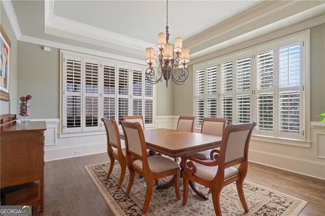 dining room with crown molding, wood finished floors, a raised ceiling, a wainscoted wall, and a chandelier