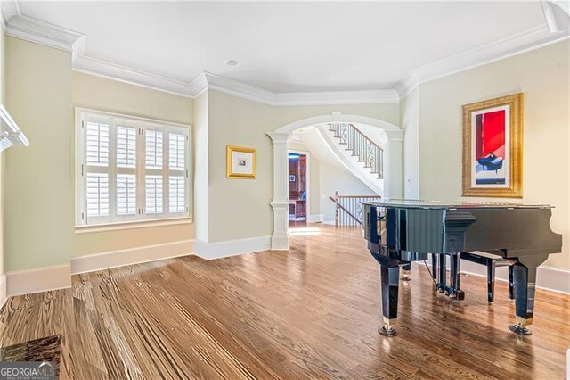 living area with decorative columns, crown molding, arched walkways, wood finished floors, and baseboards