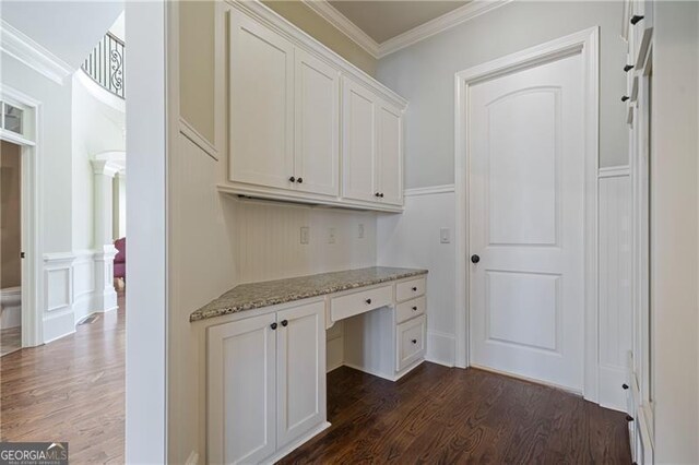 unfurnished office featuring built in study area, dark wood finished floors, crown molding, and a decorative wall