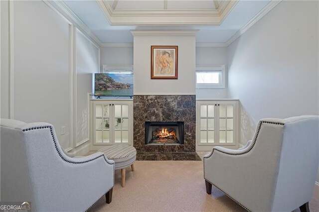 living area with a raised ceiling, a premium fireplace, ornamental molding, and carpet