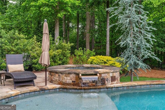view of pool featuring a patio, a pool with connected hot tub, and a wooded view