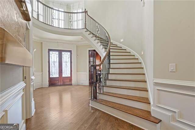entryway featuring a high ceiling, wainscoting, a decorative wall, french doors, and stairway
