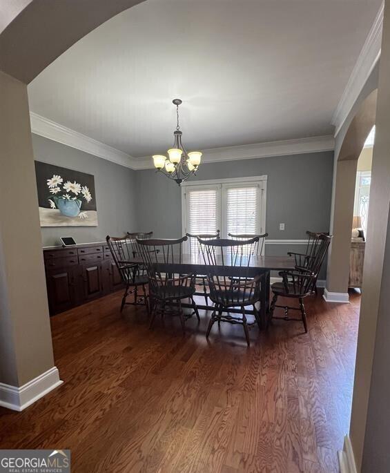 2973 Red Fox Dr, Haddock, GA 31033 - dining room featuring arched walkways, dark wood-style flooring, crown molding, a chandelier, and baseboards