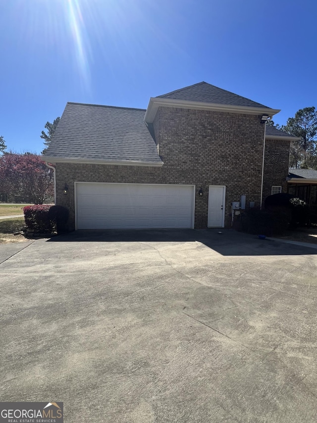 2973 Red Fox Dr, Haddock, GA 31033 - view of side of home with driveway, brick siding, an attached garage, and roof with shingles