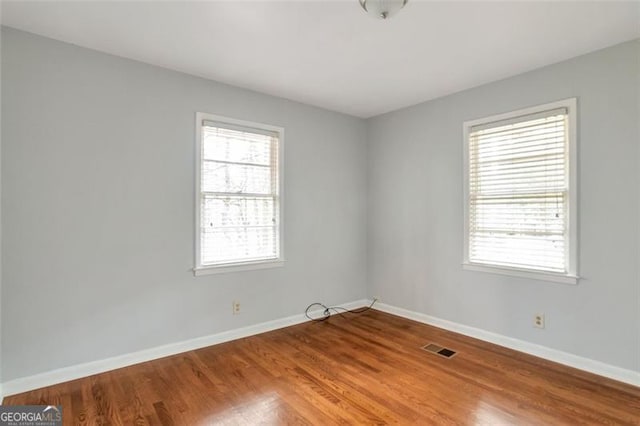 spare room featuring visible vents, wood finished floors, baseboards, and a wealth of natural light