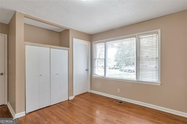 unfurnished bedroom featuring baseboards, wood finished floors, visible vents, and a closet