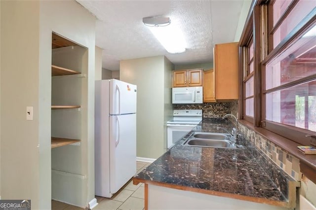 kitchen featuring a sink, dark stone countertops, a textured ceiling, white appliances, and light tile patterned floors