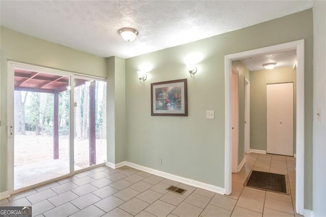 spare room with baseboards, light tile patterned flooring, a textured ceiling, and visible vents