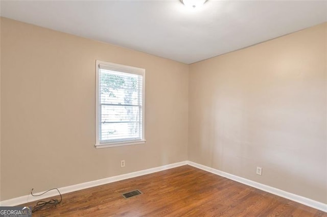 empty room featuring baseboards, wood finished floors, and visible vents
