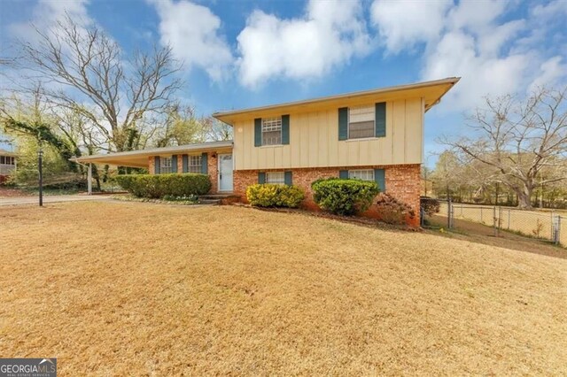 split level home featuring driveway, an attached carport, fence, brick siding, and a front lawn