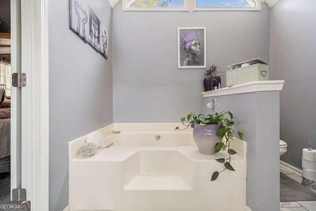 bathroom with a garden tub, connected bathroom, and toilet