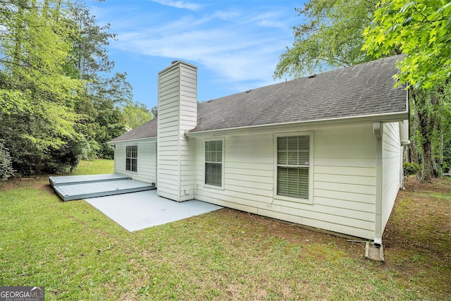 rear view of property featuring a shingled roof, a patio area, a yard, and a chimney