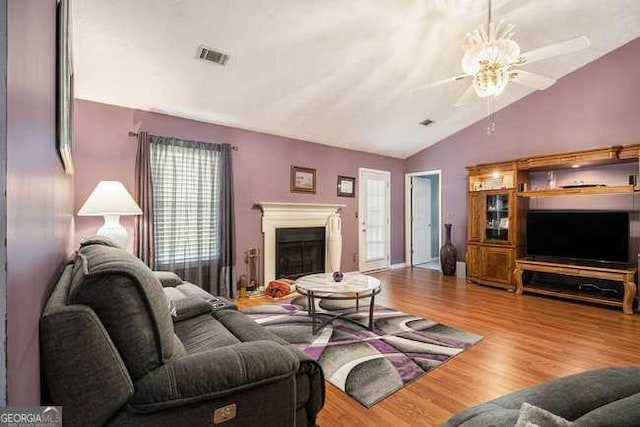 living area with visible vents, a glass covered fireplace, lofted ceiling, wood finished floors, and a ceiling fan