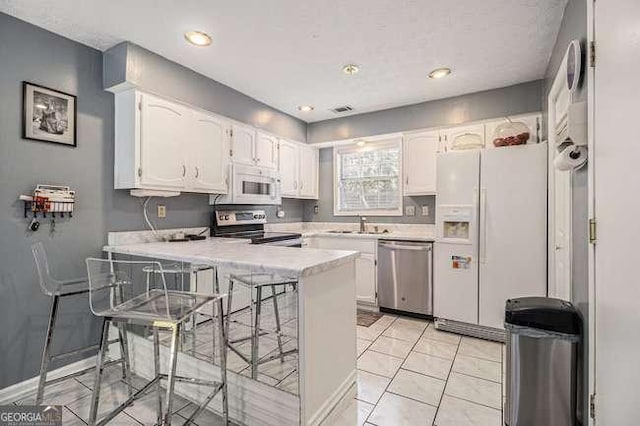 kitchen with appliances with stainless steel finishes, light countertops, white cabinets, a peninsula, and a breakfast bar