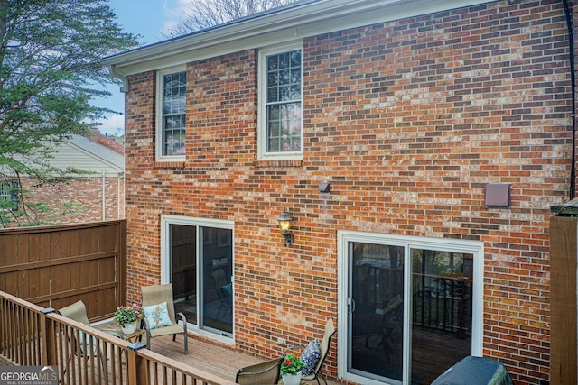rear view of property featuring fence, a wooden deck, and brick siding