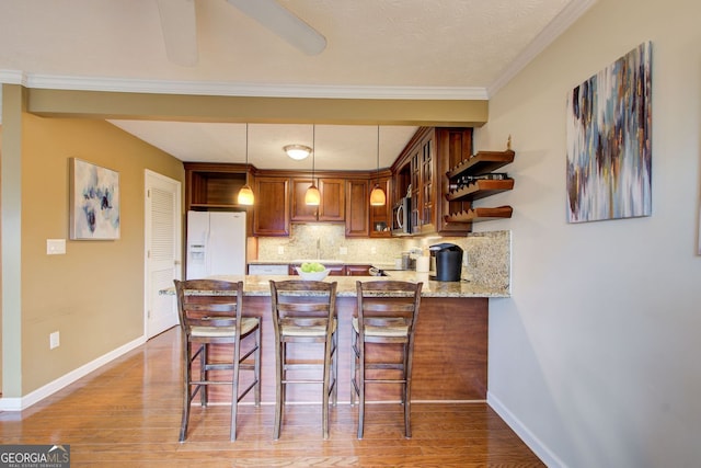 kitchen with tasteful backsplash, white refrigerator with ice dispenser, light wood finished floors, stainless steel microwave, and a peninsula