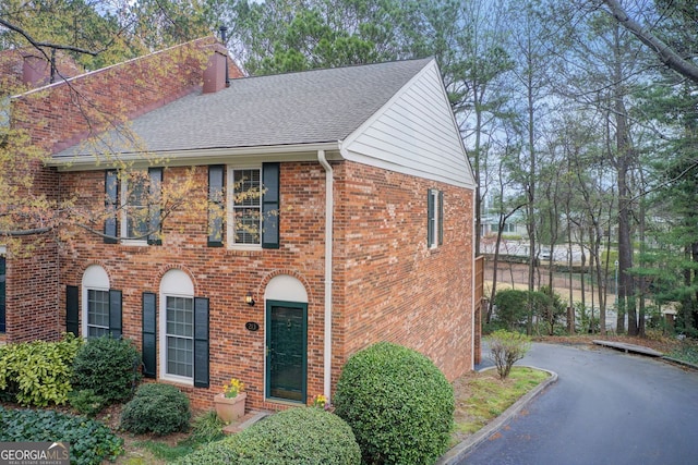 view of front of property with a chimney, brick siding, and roof with shingles