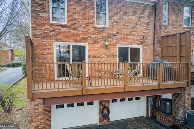 back of house with brick siding, an attached garage, central AC, and aphalt driveway